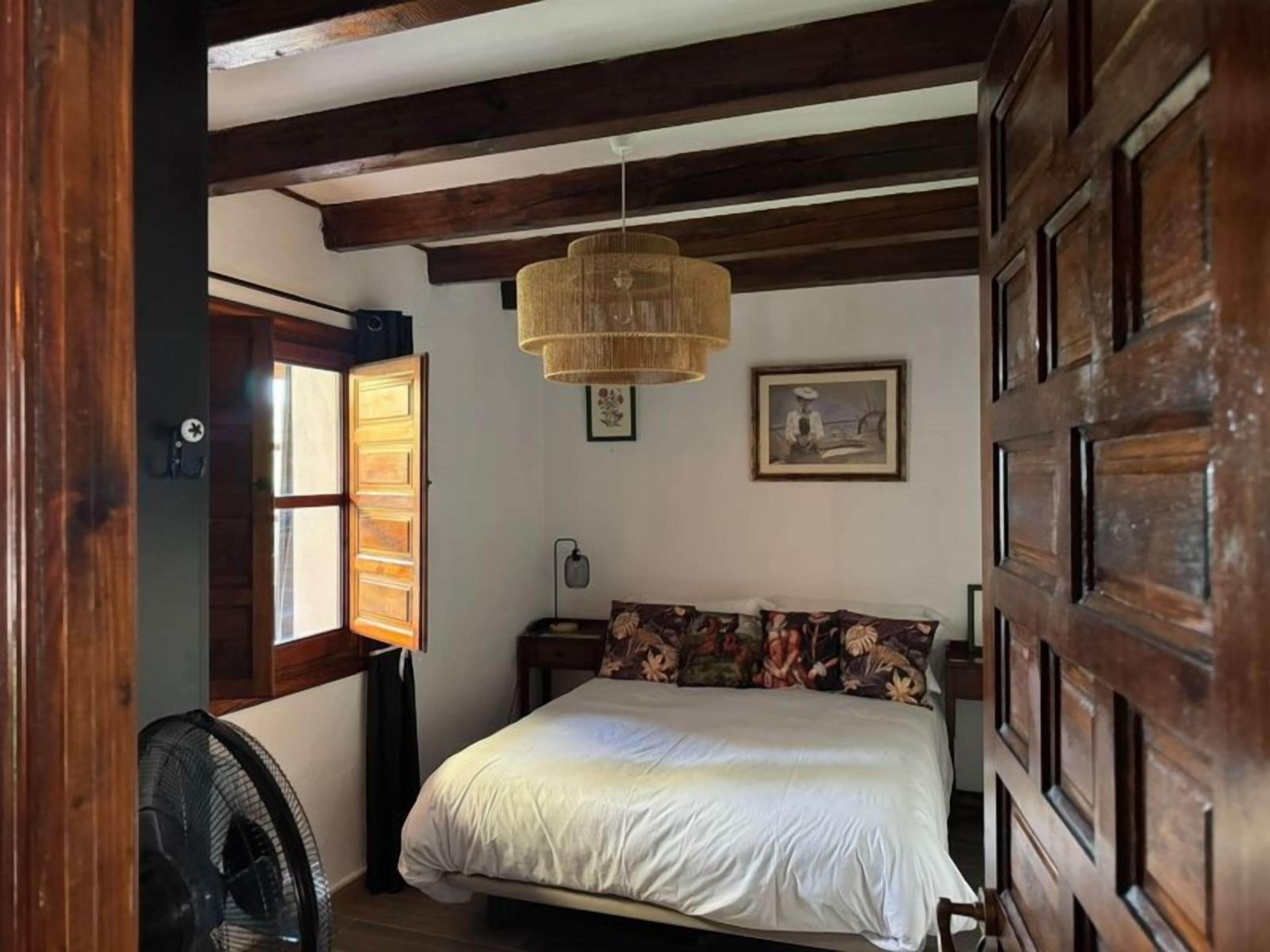 A bedroom with a bed, a fan, a window, and a door.