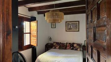 A bedroom with a bed, a fan, a window, and a door.