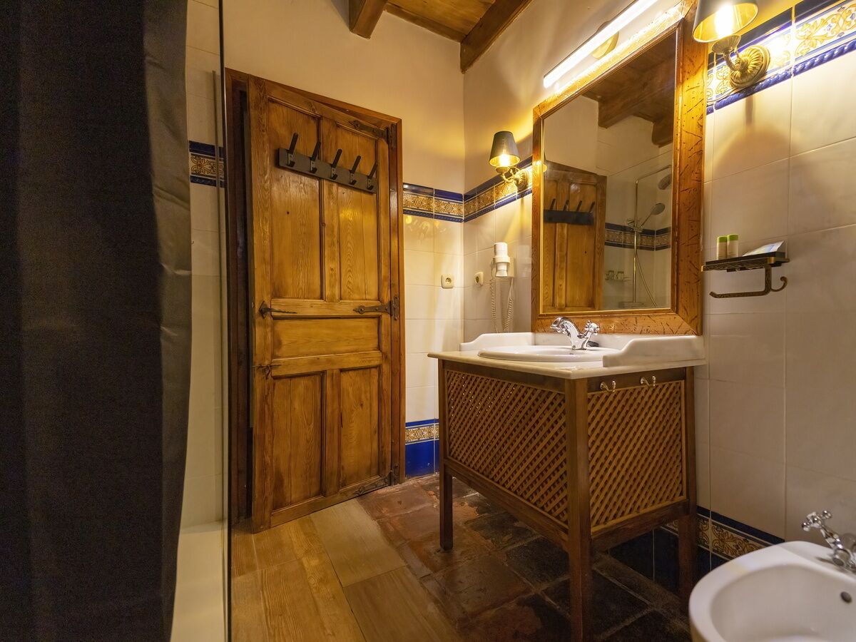 A bathroom with a wooden door, a sink, a mirror, and a shower area.