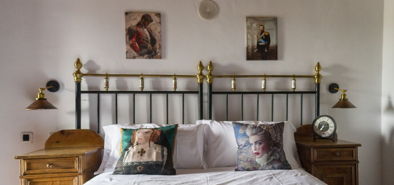 Un dormitorio con cabecera de metal negro, dos mesitas de noche con lámparas y dos almohadas con retratos.