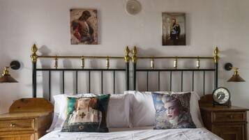 Un dormitorio con cabecera de metal negro, dos mesitas de noche con lámparas y dos almohadas con retratos.