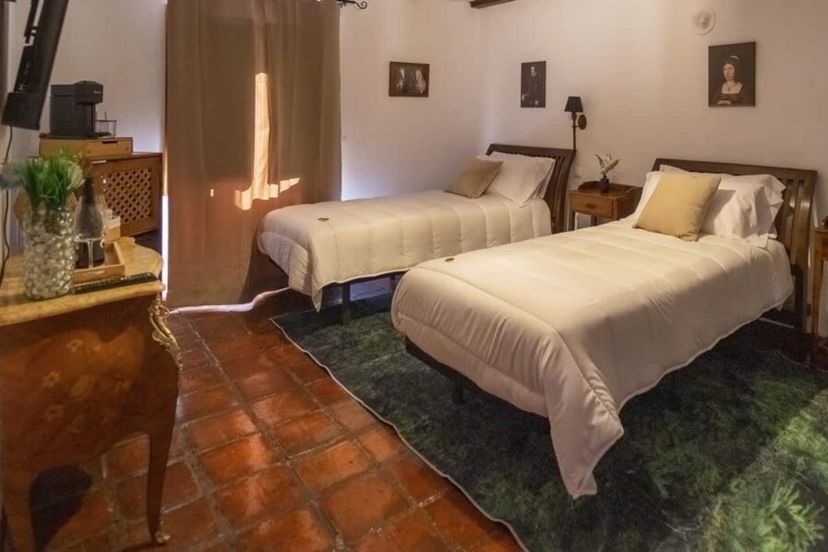 Une chambre avec deux lits, un fauteuil vert, une table de chevet en bois et une petite table avec une lampe.
