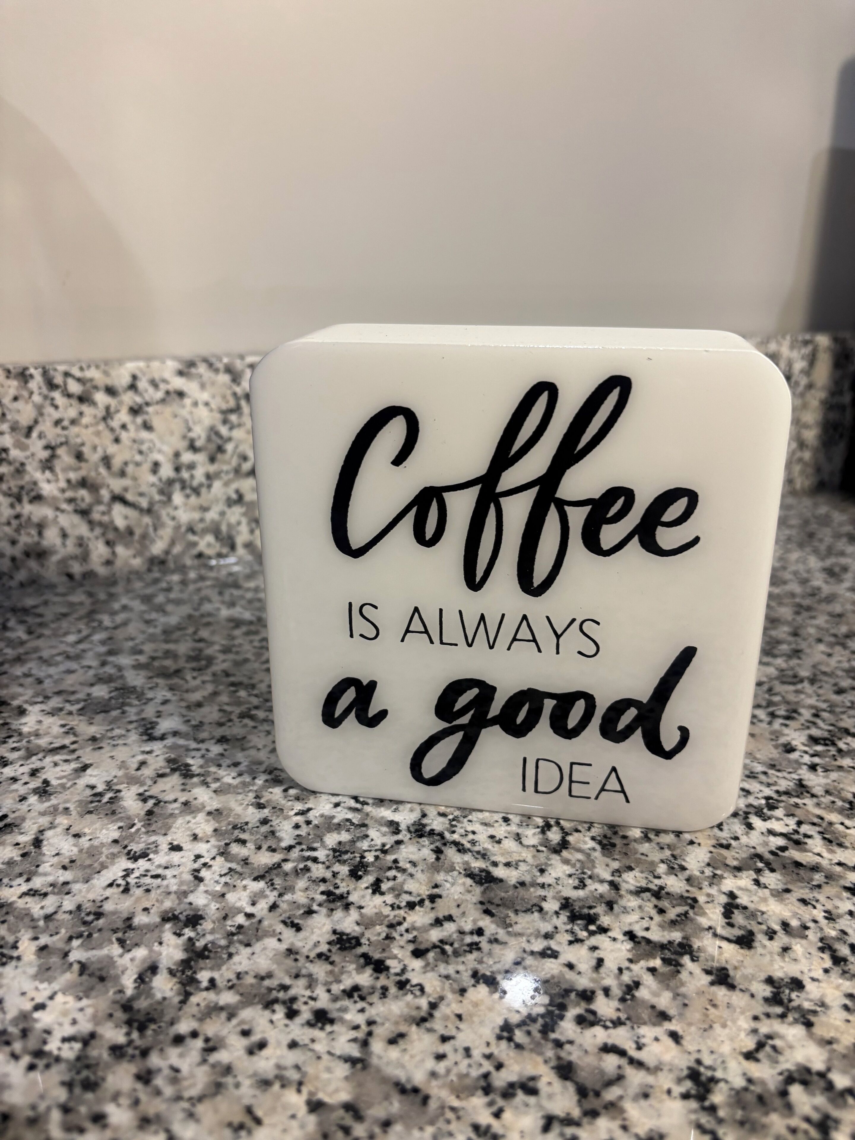 A white square sign with black text on a granite countertop.