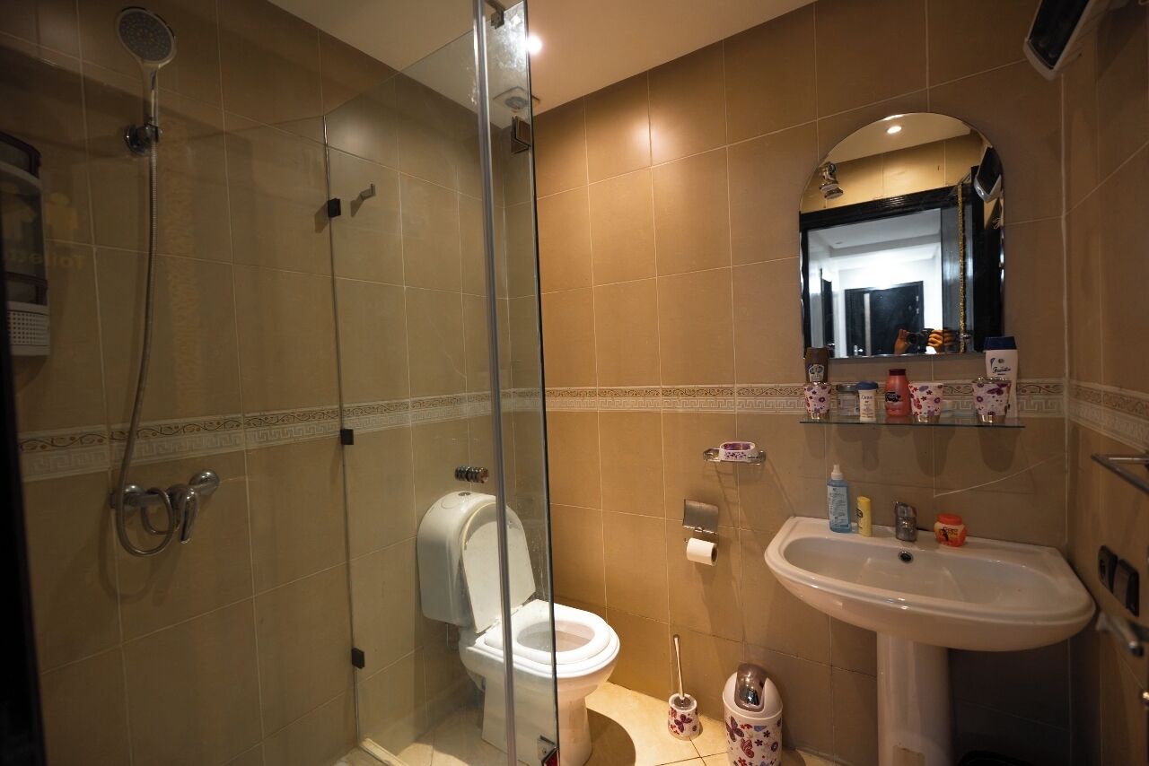 A bathroom with a glass-enclosed shower, a toilet, and a sink with a mirror above it.