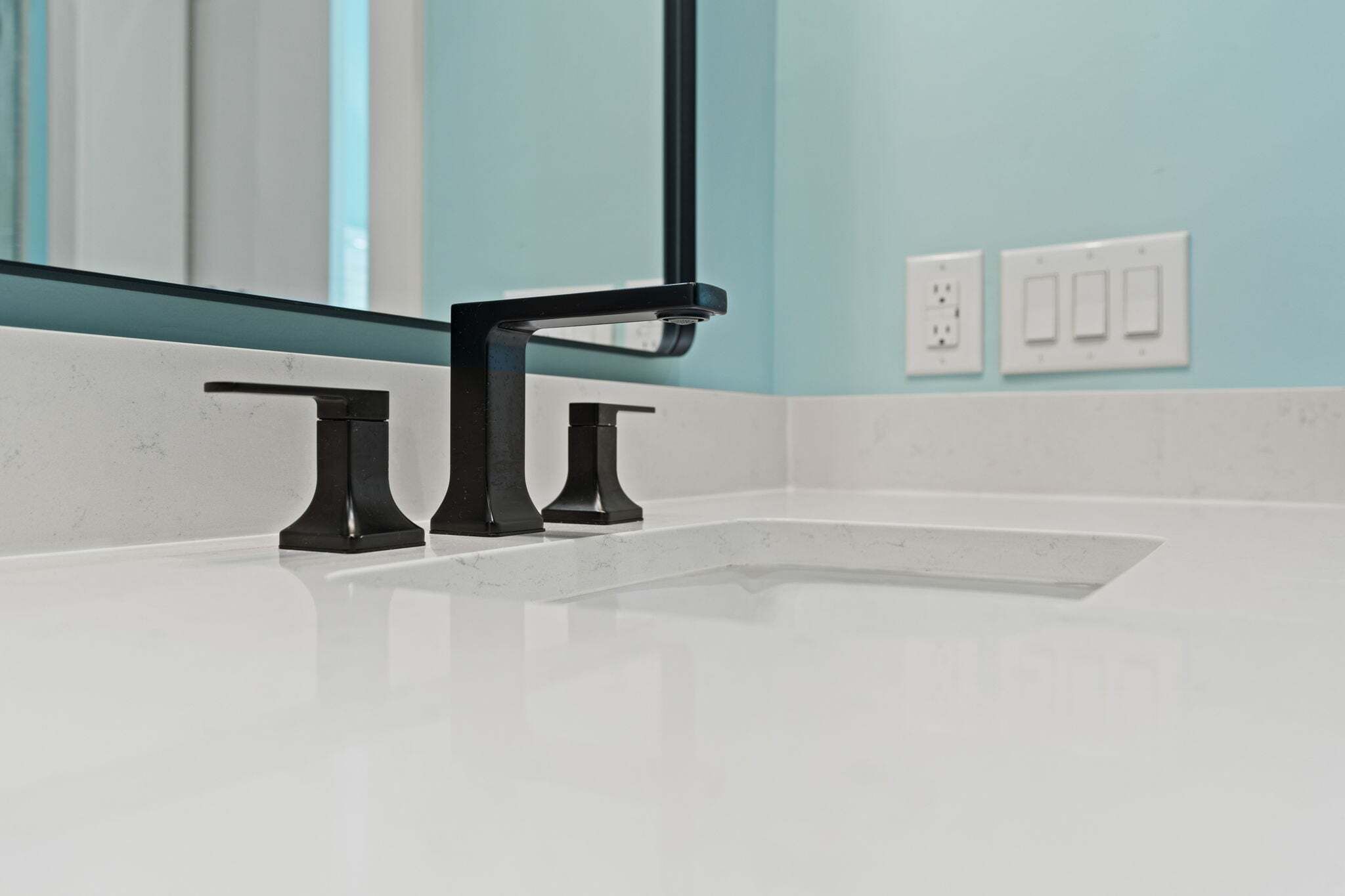 Un baño con lavamanos blanco, grifo negro y un espejo.