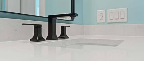 Un baño con lavamanos blanco, grifo negro y un espejo.