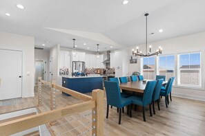 A modern kitchen with white cabinets, a central island, and a dining area with blue chairs. - 5228 E Beach Dr, perfect for 18 guests with a pool and dog-friendly amenities. (Oak Island)