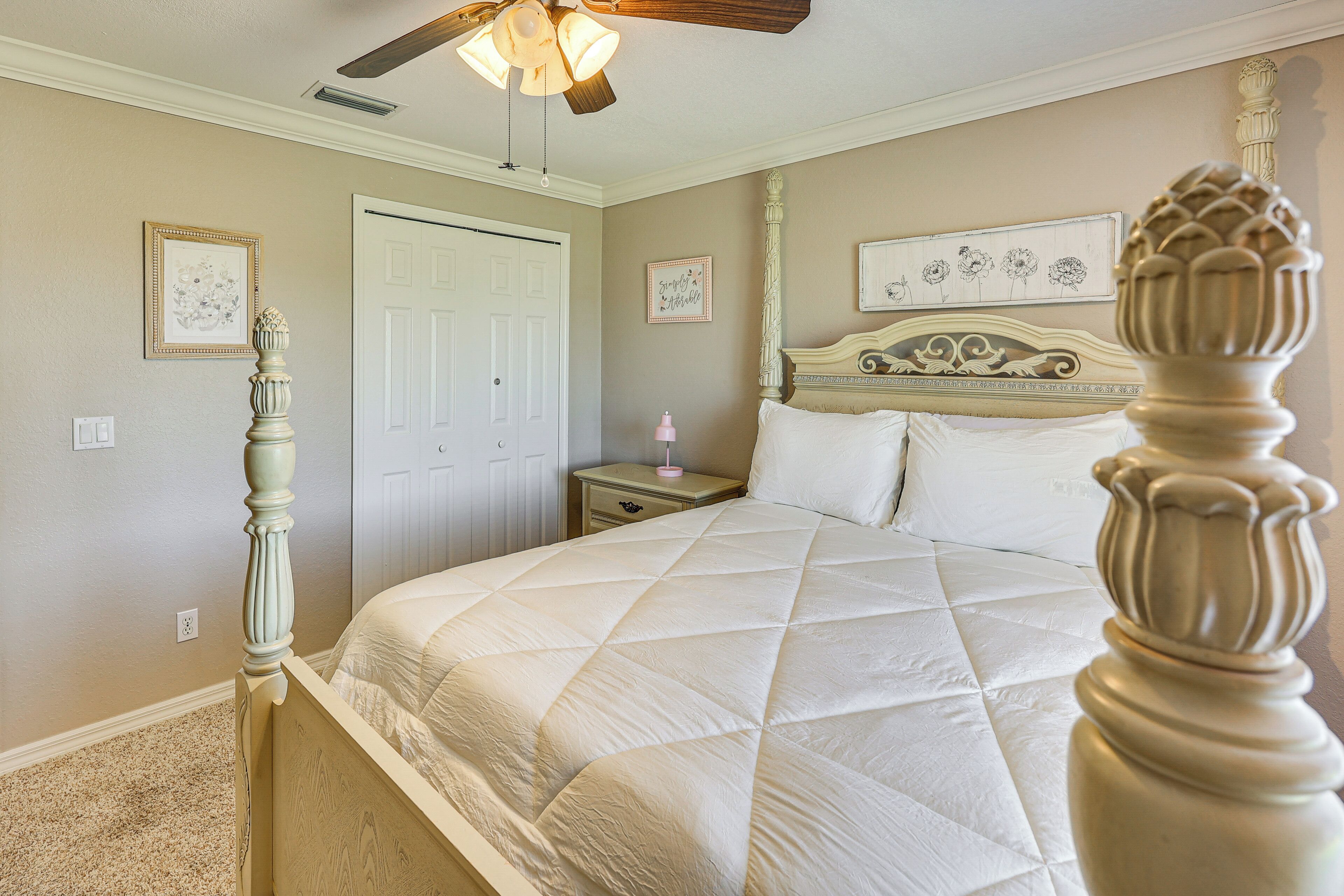 A bedroom with a bed, a nightstand, a dresser, a ceiling fan, and a door.