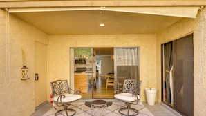 A covered patio with two chairs and a table, a fire extinguisher, and a sliding glass door leading to an interior space. - Walk to Canal Trail! Condo w/ Pool in Scottsdale (Scottsdale)