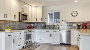 Eine moderne Küche mit weißen Schränken, Edelstahlgeräten, einer Steinrückwand und Holzboden.