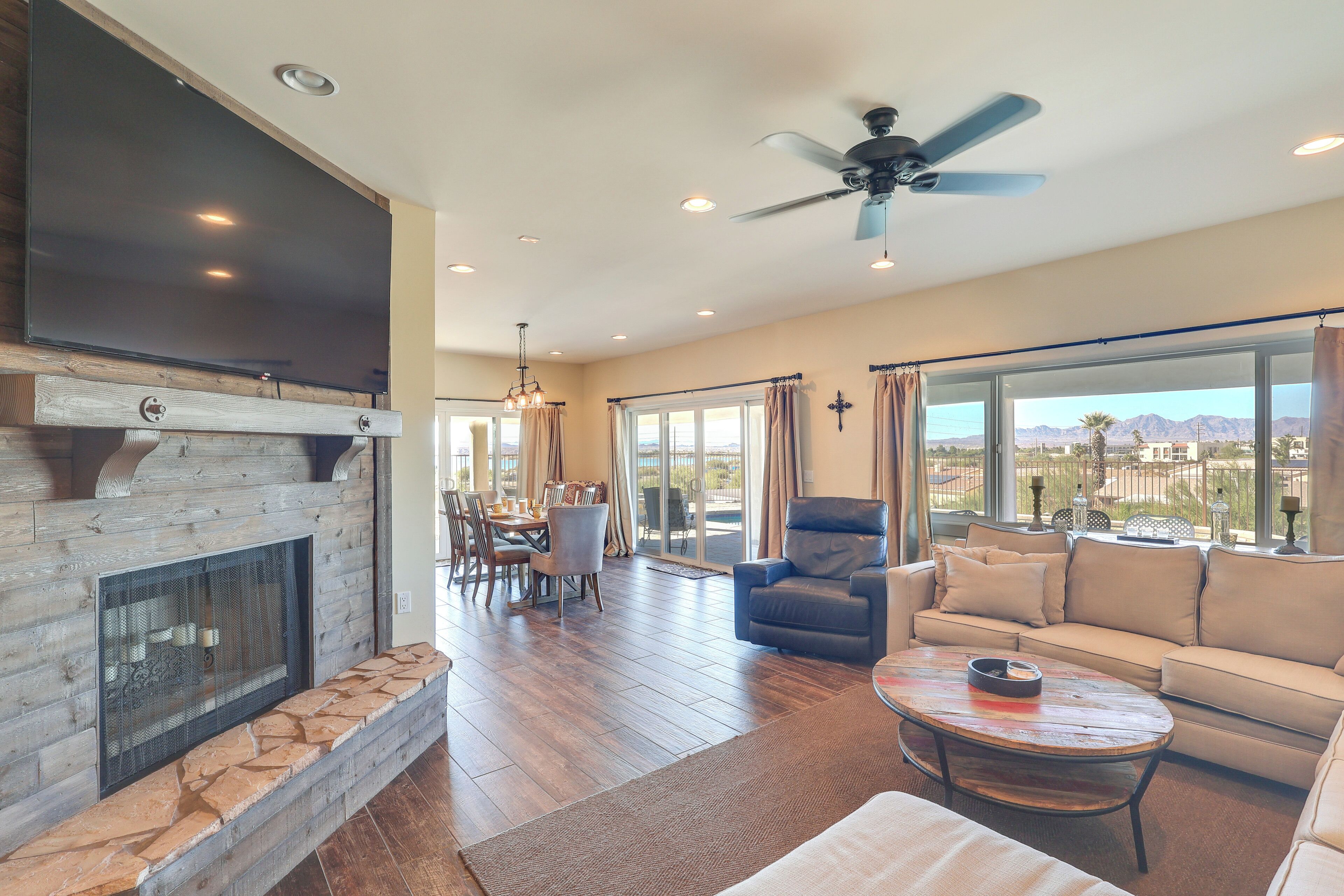 A spacious living room with a fireplace, a large TV, a ceiling fan, and a view of the mountains through the windows.