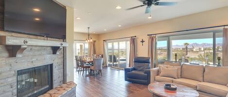 A spacious living room with a fireplace, a large TV, a ceiling fan, and a view of the mountains through the windows.