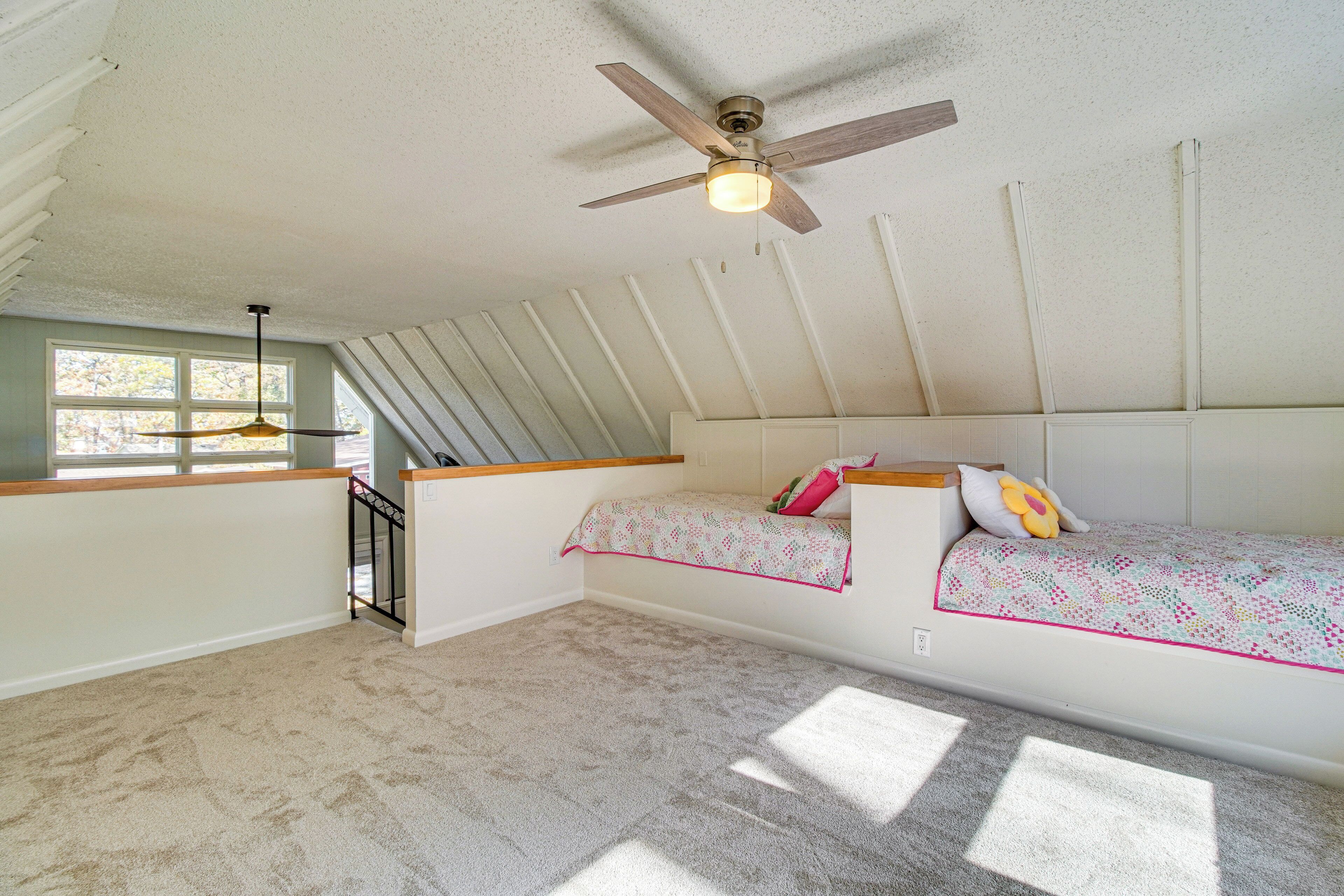 A bedroom with a sloped ceiling, a ceiling fan, a window, and a bed with a patterned bedspread.