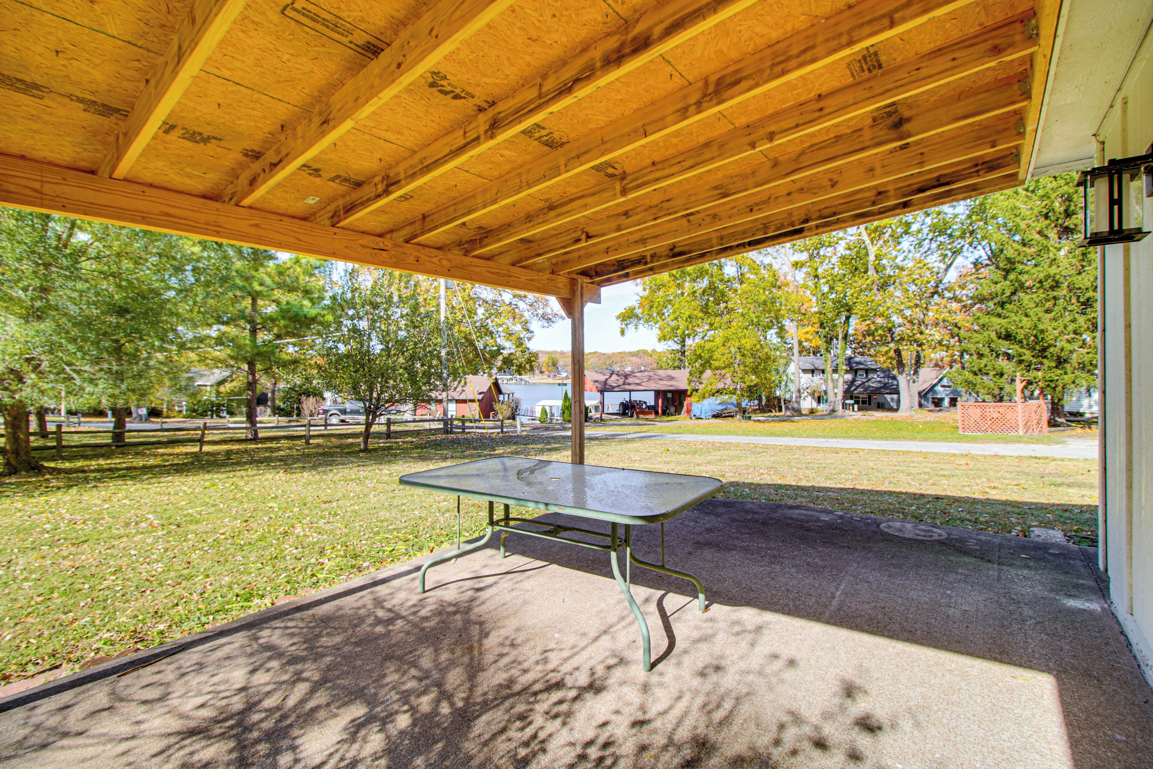 An outdoor covered area with a picnic table, surrounded by grass and trees.