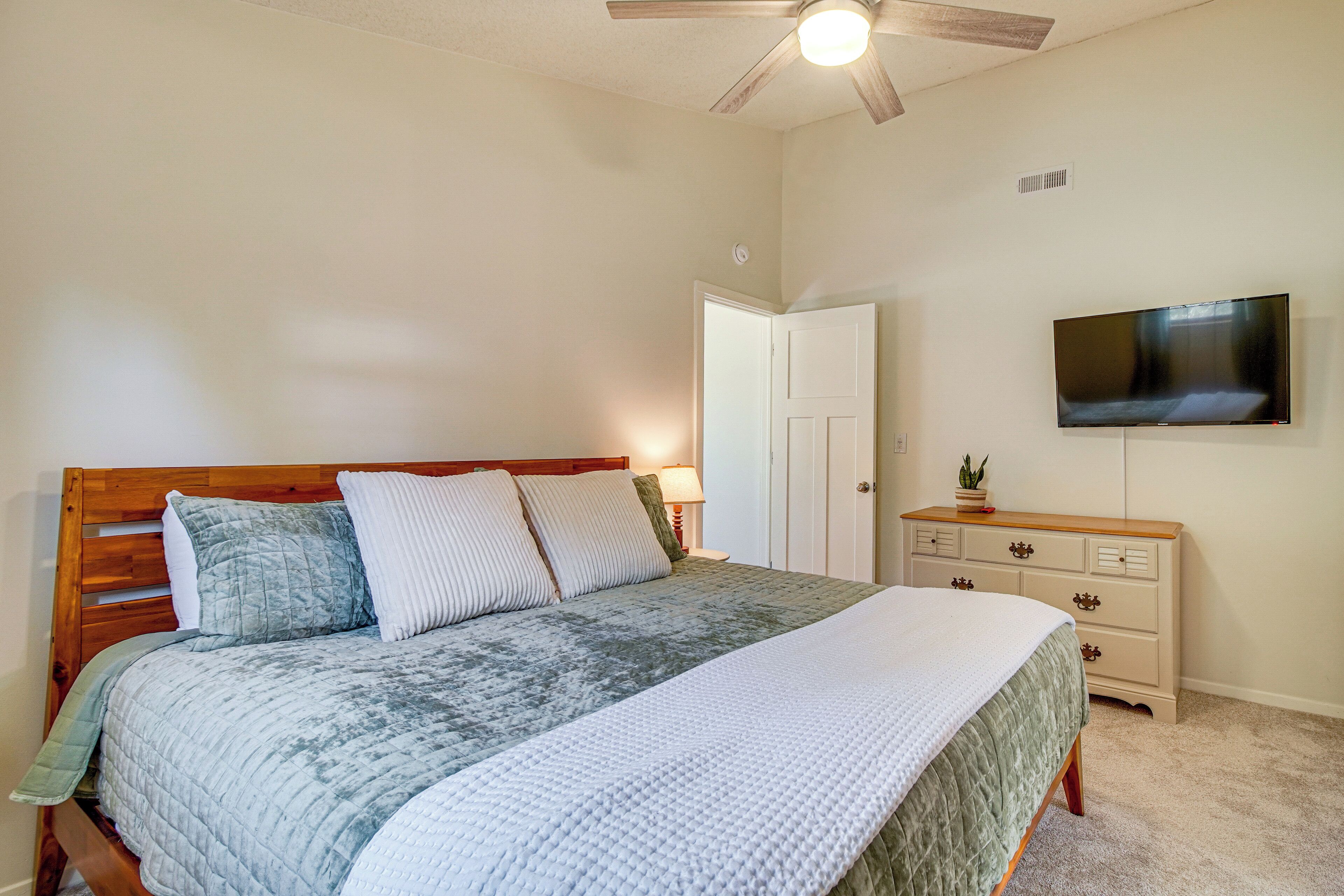 A bedroom with a wooden bed, a flat-screen TV, a dresser, and a ceiling fan.