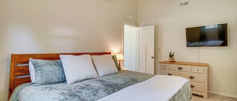 A bedroom with a wooden bed, a flat-screen TV, a dresser, and a ceiling fan.