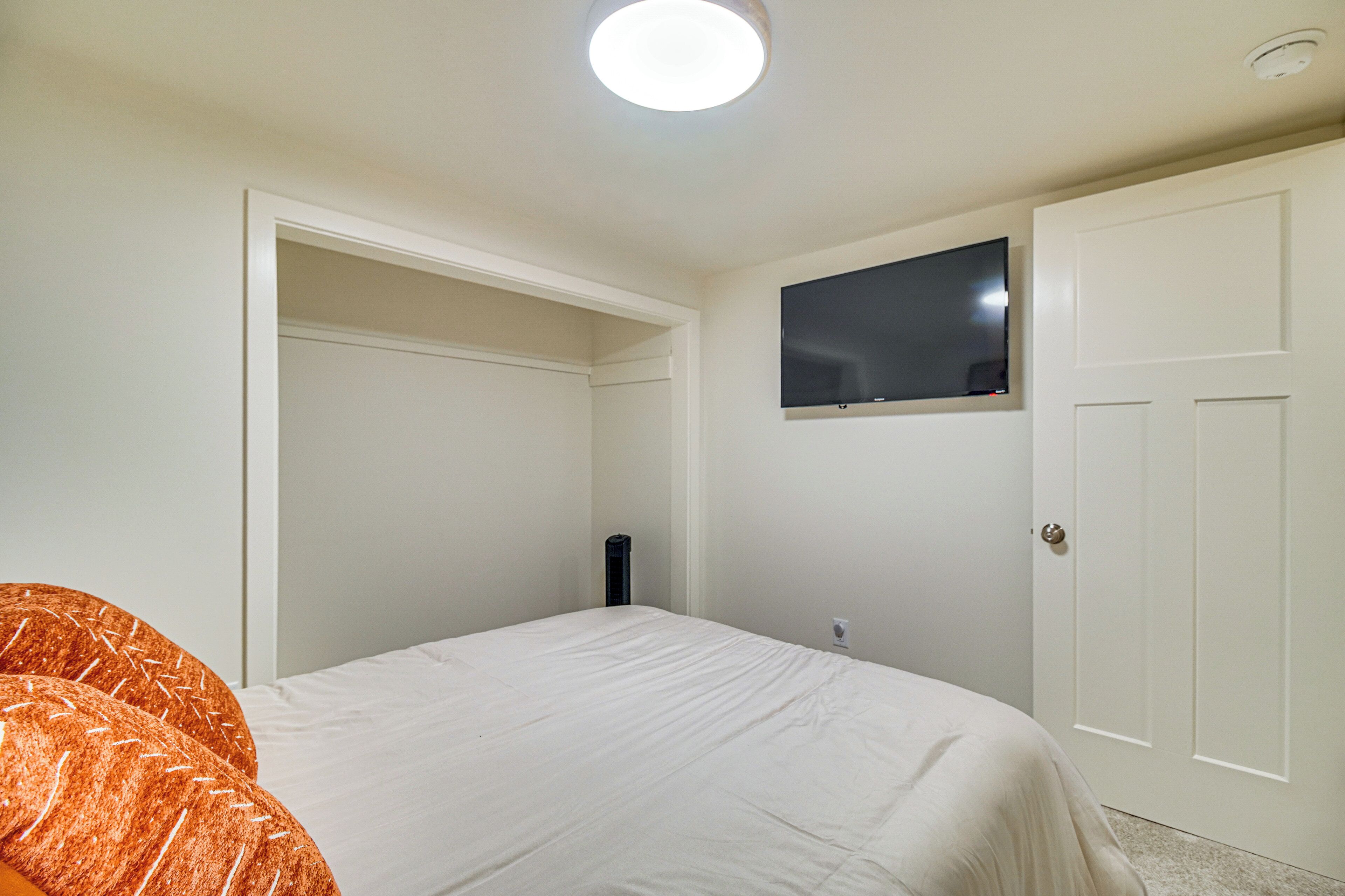 A bedroom with a bed, a television mounted on the wall, and a white door.
