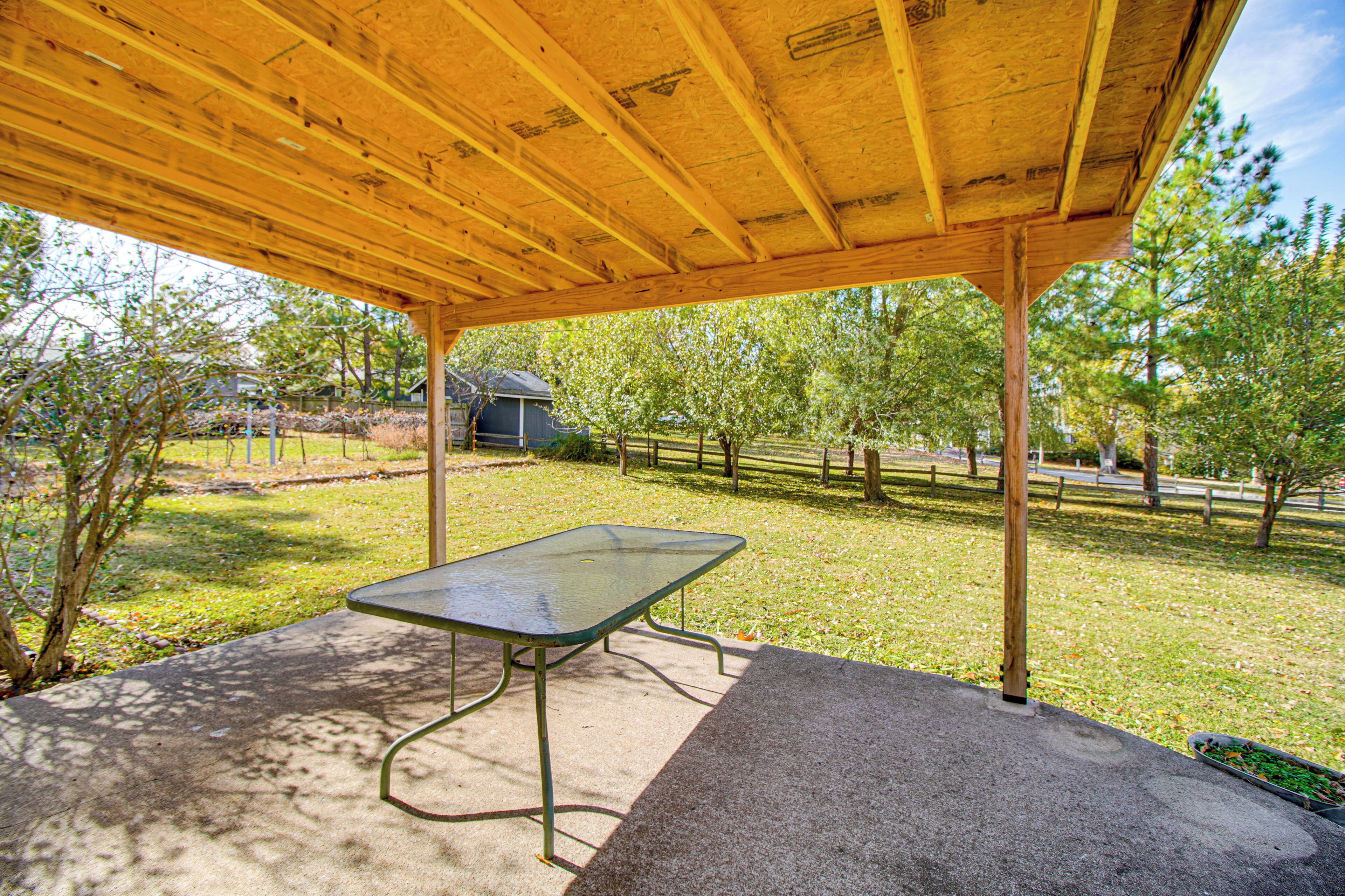 A covered picnic table in a park with a wooden roof and concrete ground.