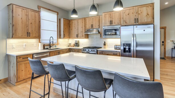 A modern kitchen with wooden cabinets, a large island with bar stools, stainless steel appliances, and pendant lighting. - 5 Mi to Winter Park Skiing & Dtwn: Mtn-view Condo (Fraser)