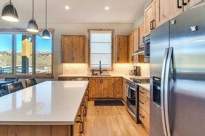 A modern kitchen with wooden cabinets, a large island, stainless steel appliances, and a view of the mountains through the windows. - 5 Mi to Winter Park Skiing & Dtwn: Mtn-view Condo (Fraser)