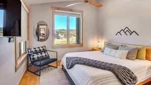 A bedroom with a large bed, a ceiling fan, a window with a view, a chair, and a mounted TV. - 5 Mi to Winter Park Skiing & Dtwn: Mtn-view Condo (Fraser)