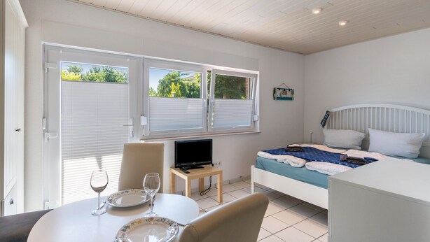 Une chambre à coucher avec un lit, une télévision, une petite table avec un verre, et une table à manger.