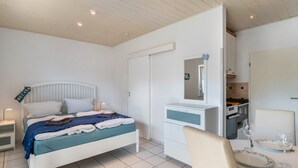 Une chambre à coucher comprenant un lit, une table de chevet, une commode, un miroir, ainsi qu’un coin repas avec une table et des chaises.