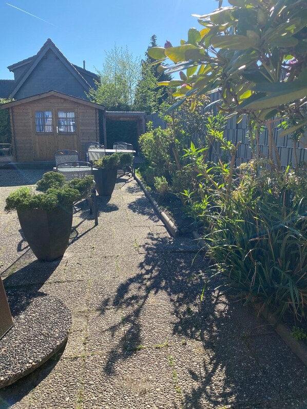 A wooden cabin with a gravel path, potted plants, and a metal table and chairs. - Apartment, 20 sqm, living/sleeping area with kitchenette, private terrace, max. 2 guests (Wangerland)