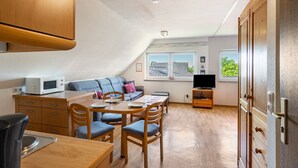 Et lille køkken med spisebord, stole, mikrobølgeovn og fjernsyn.