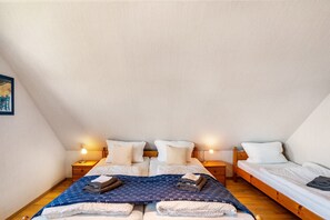 A bedroom with two beds, a wooden floor, and bedside lamps. - Apartment, 30 sqm, 1 living/sleeping room, max 3 guests (Wangerland)