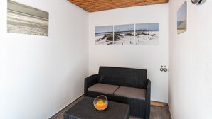 Ein Zimmer mit Holzboden, einer schwarzen Rattan-Couch, einem kleinen Tisch mit einer Glaskugel und drei gerahmten Bildern an der Wand.