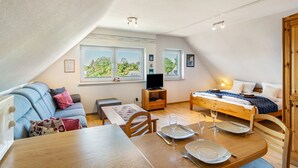Et hyggeligt loftværelse med seng, fjernsyn, spisebord og sofa.