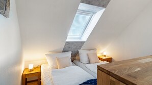 Een slaapkamer met dakraam, twee nachtkastjes met lampen, een bed met wit beddengoed en een houten dressoir.