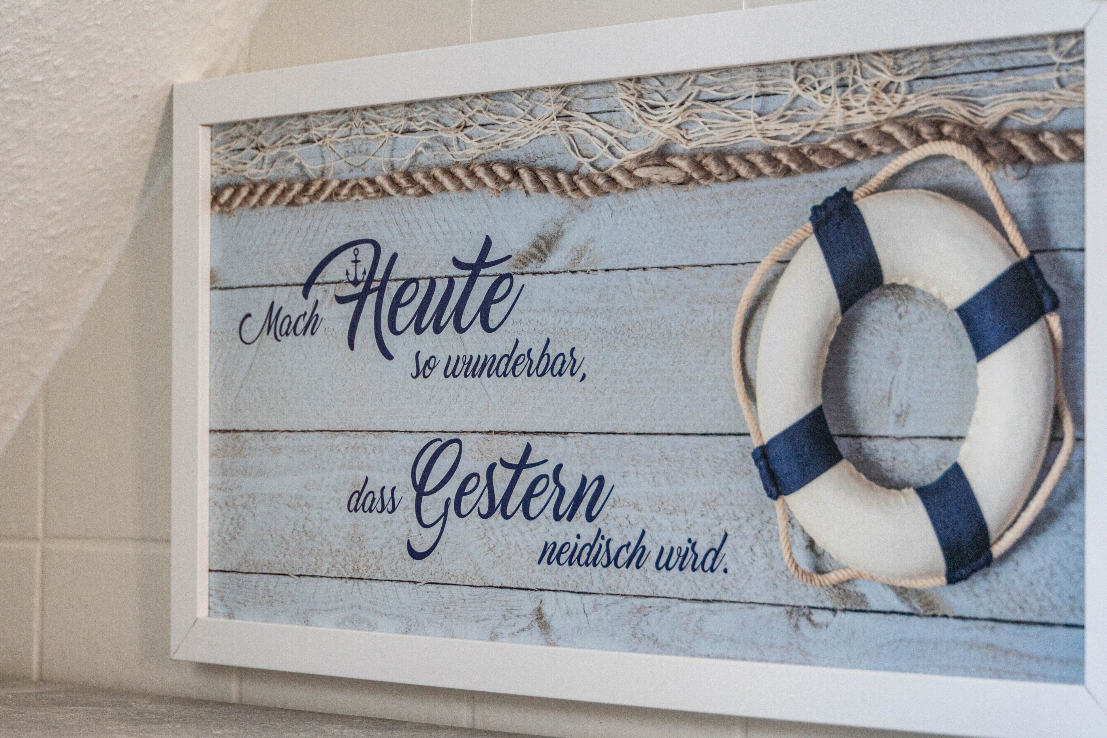 Ein gerahmtes Schild im maritimen Stil, mit einem Rettungsring und Schrift in einer Fremdsprache.