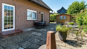 Tiilitalo, jossa on patio, ulkotila istumista varten ja taustalla puinen rakennelma.