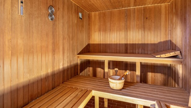 Sauna, jonka seinät ovat puuta, siinä on penkki, ämpäri ja kaksi metallista astiaa.