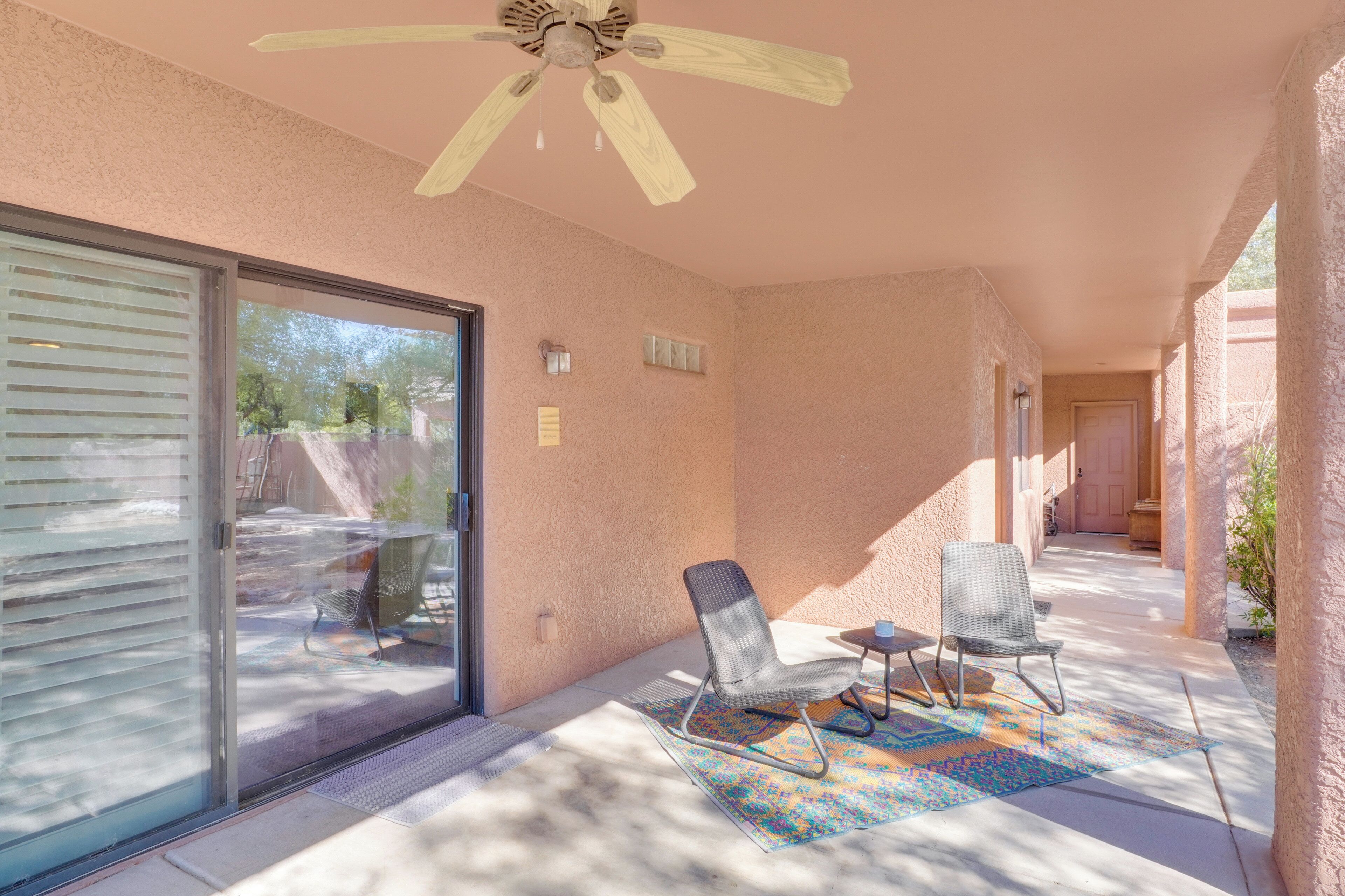 A covered patio with a ceiling fan, sliding glass door, and two chairs.