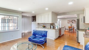 A spacious living area with a blue leather sofa, a glass coffee table, and a kitchen in the background. - 5 Mi to Lake Accotink Park: Modern Home w/ Yard (Springfield)