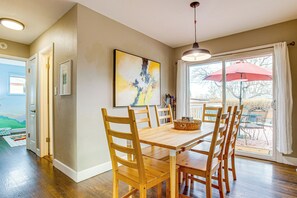 A dining area with a wooden table and chairs, a large abstract painting on the wall, and a view through a glass door to an outdoor patio with umbrellas. - Easy I-25 Access! Vibrant North Denver Home (Denver)