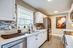 A modern kitchen with white cabinets, a stainless steel refrigerator, and a large window with blinds. - Easy I-25 Access! Vibrant North Denver Home (Denver)