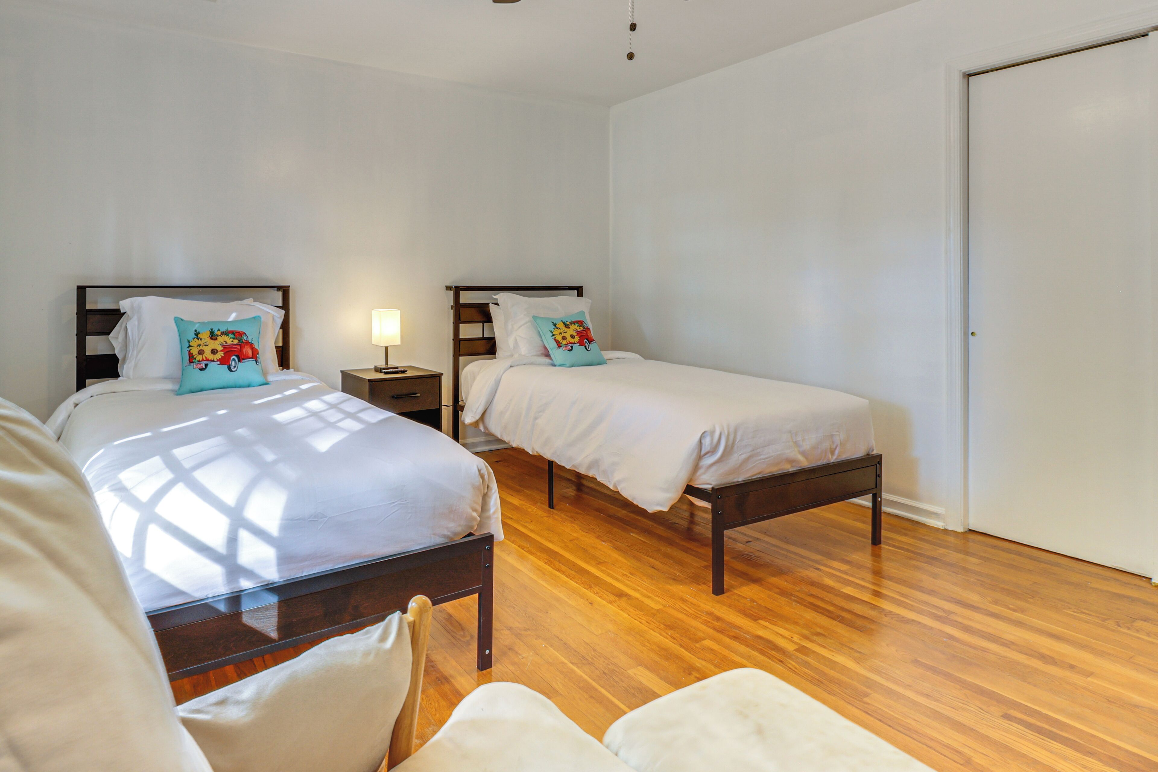 Habitación de hotel con dos camas individuales, piso de madera, paredes blancas y una puerta cerrada.
