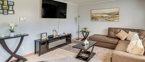 Un salon comprenant un téléviseur à écran plat, un canapé en cuir marron, une table basse, une console et un tapis.