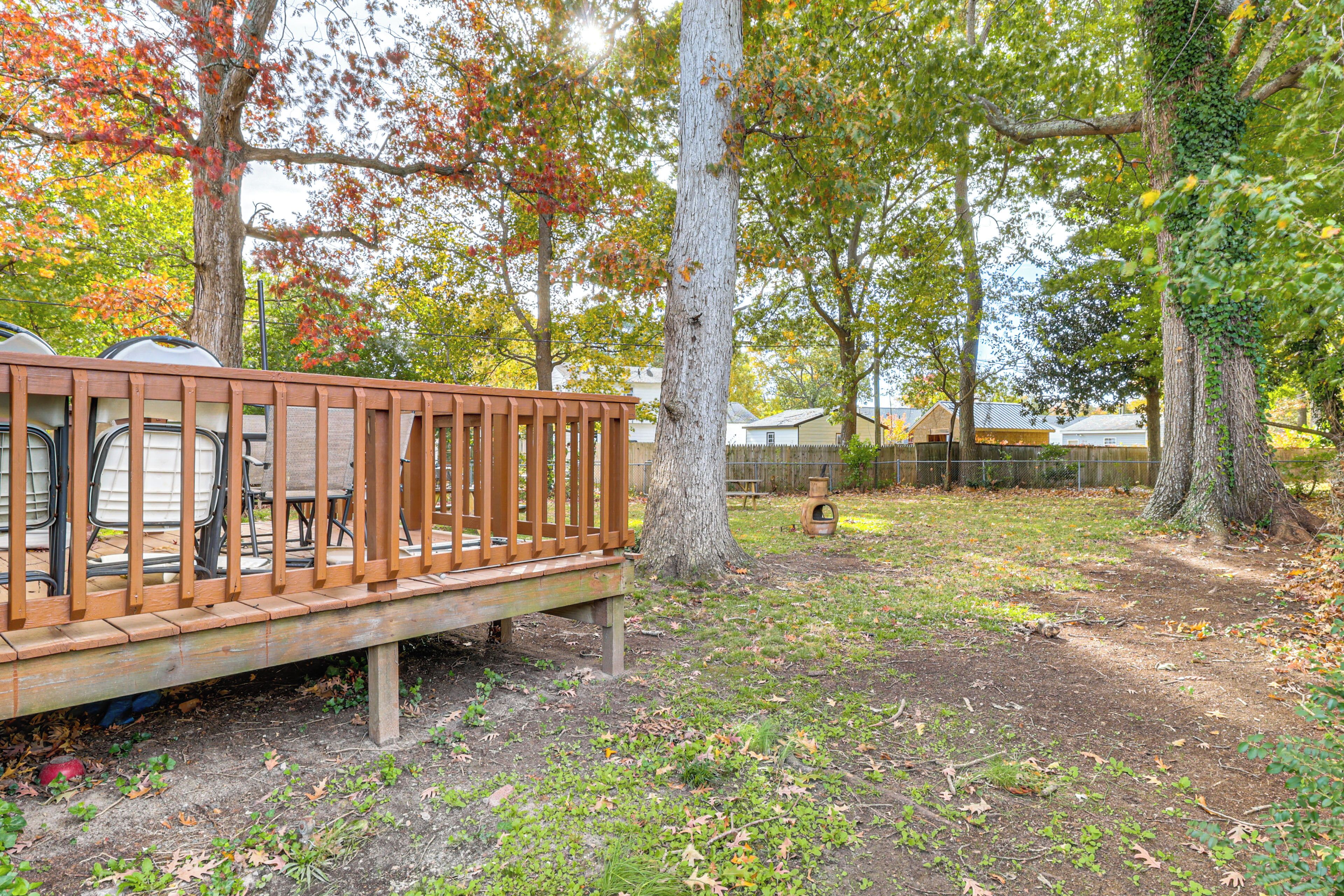 Une terrasse en bois, avec des chaises et une table, entourée d’arbres aux feuilles d’automne.