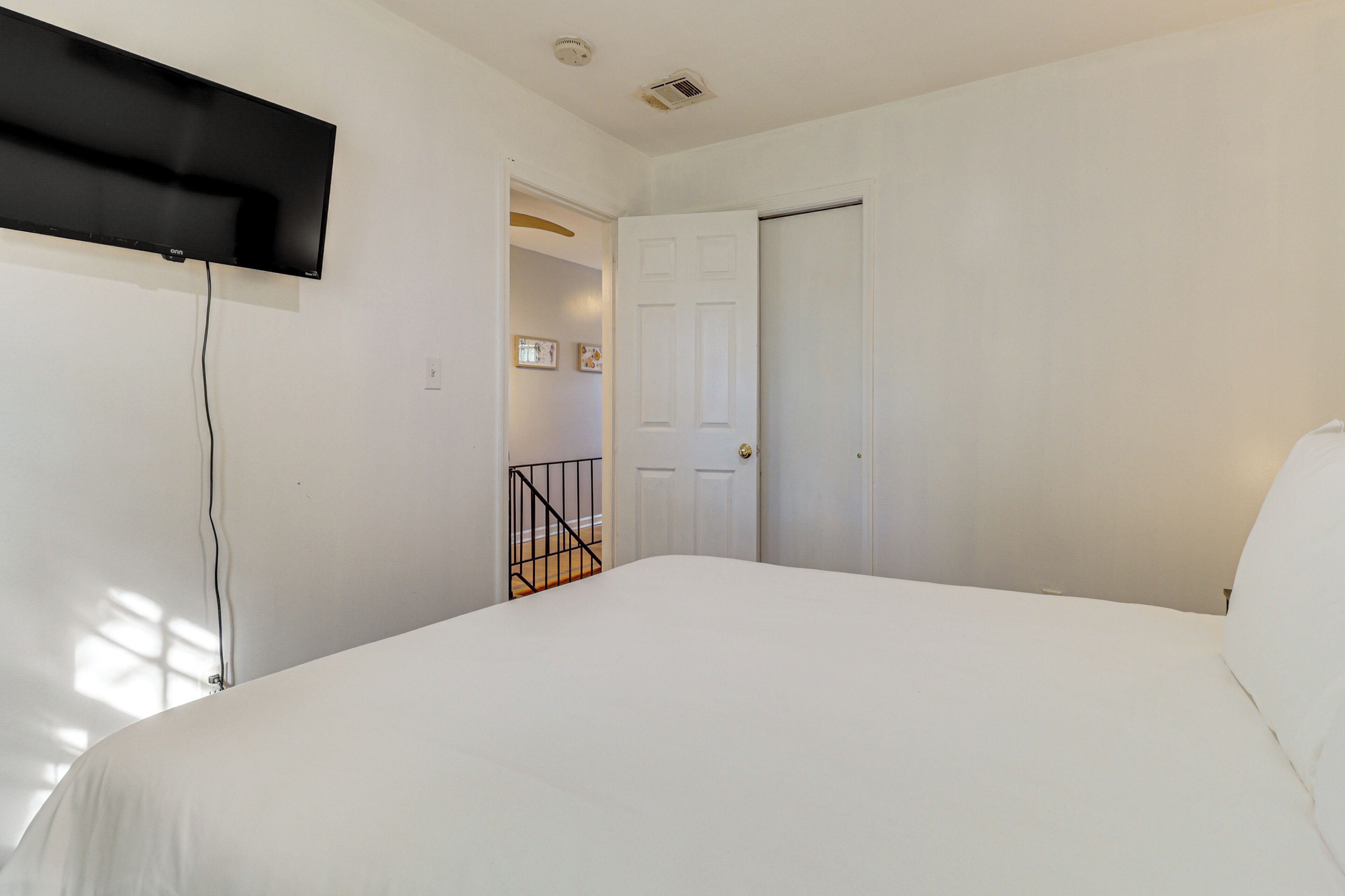 Un dormitorio con cama, televisor montado en la pared y puerta que da a otra habitación.