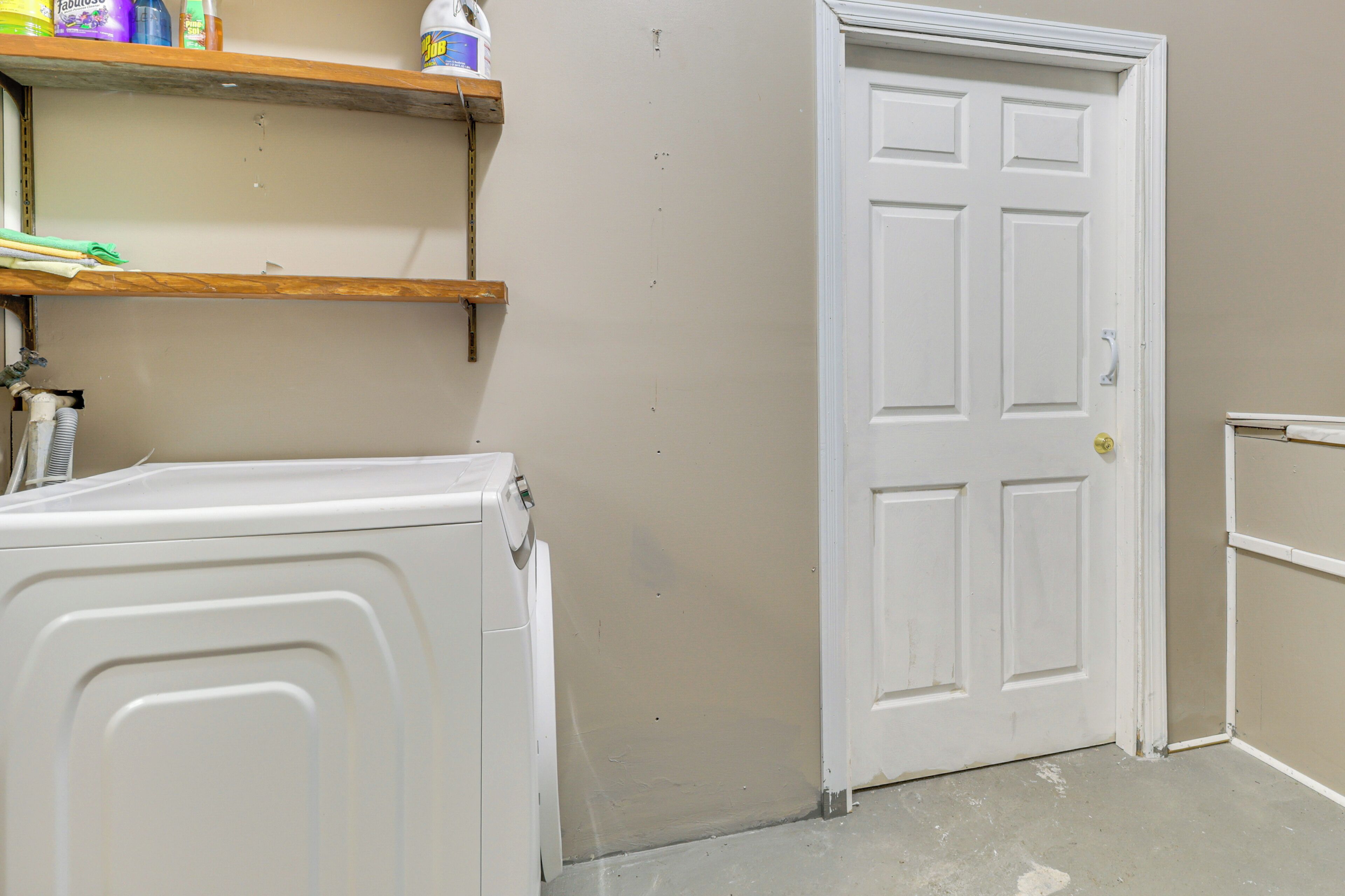 A laundry room with a white door, a washing machine, and shelves with cleaning supplies.