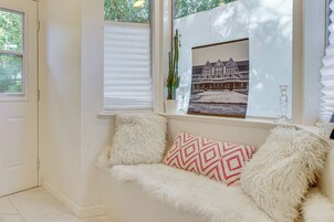 Una habitación acogedora con un sofá blanco, almohadas mullidas, un cuadro enmarcado y una ventana con persianas.