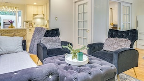A modern living room with a tufted ottoman, two dark armchairs, a small side table with a tray, and a view into the kitchen area. - Work & Relax! Updated Walnut Creek Home w/ Office (Walnut Creek)
