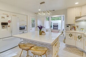 Una cocina moderna con armarios blancos, una isla central con taburetes, microondas y refrigerador.