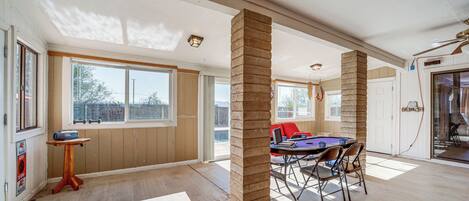 Amplia habitación con mesa de billar, una mesa de comedor con sillas y ventanas grandes que dejan entrar luz natural.