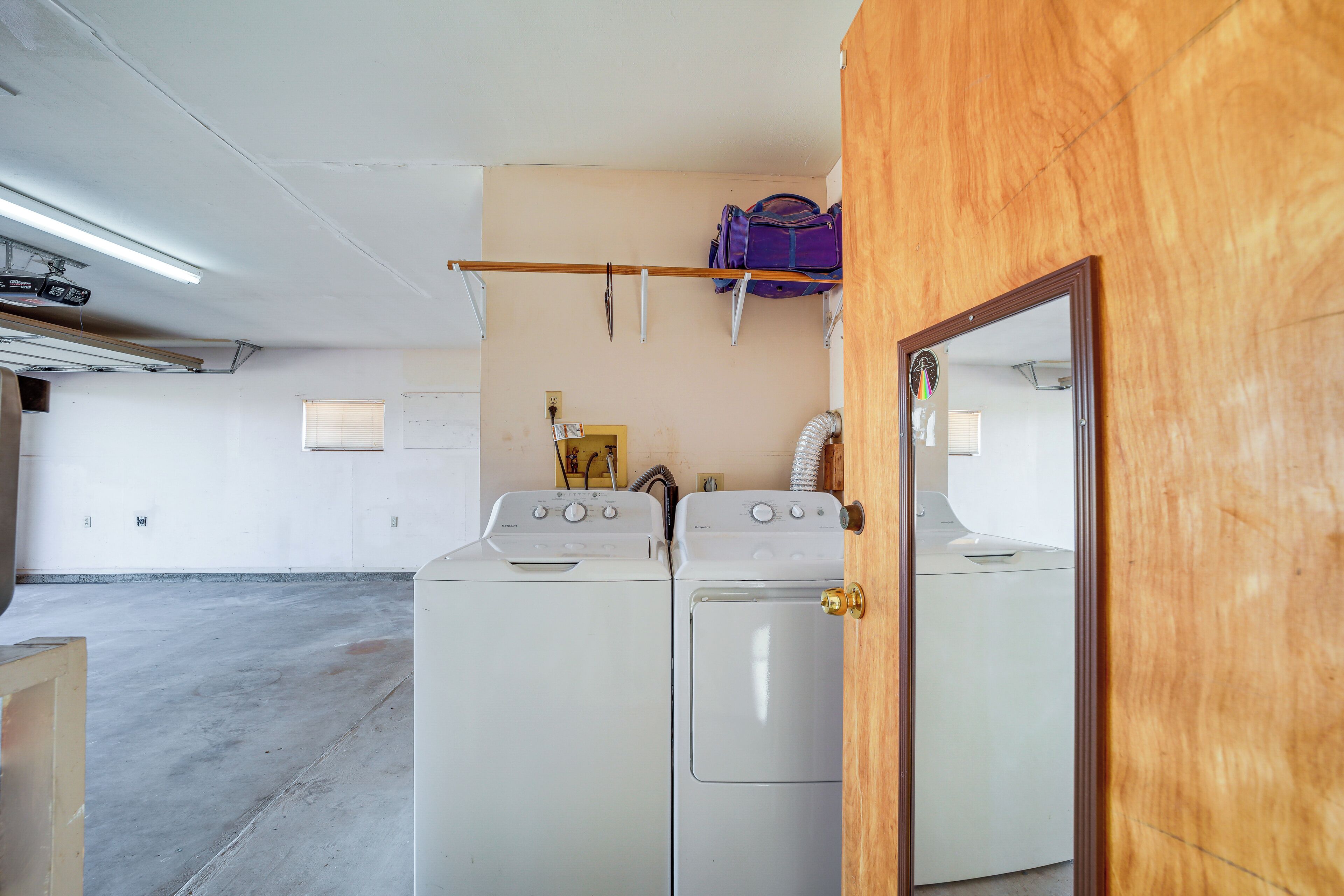 A laundry room with two washing machines, a drying rack, and a wooden door.